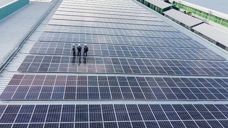 Tre montører står midt i et stort ECNergy solcelle anlæg, der er placeret på toppen af en industribygning.